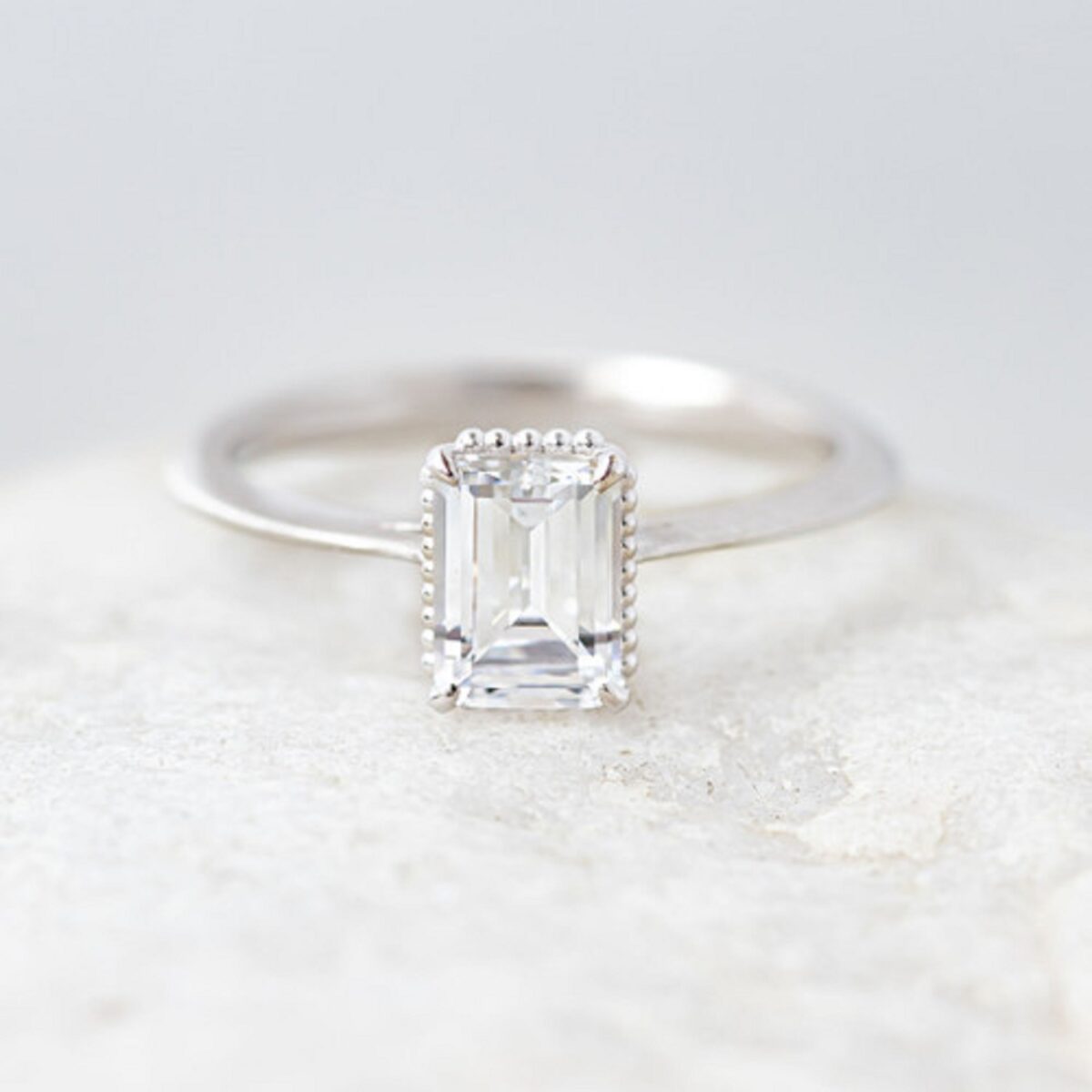 Unique hidden bead halo emerald cut solitaire ring crafted in 14k white gold.