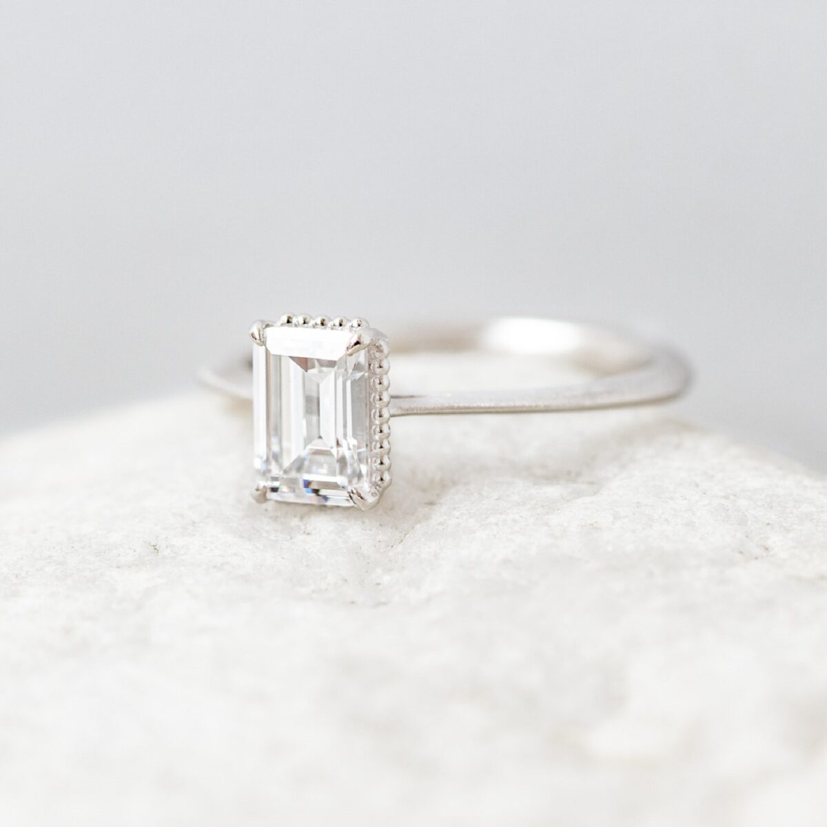 Unique hidden bead halo emerald cut solitaire ring crafted in 14k white gold.